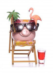 Saving money on family cruise - happy piggy bank sitting on beach chair with vacation items