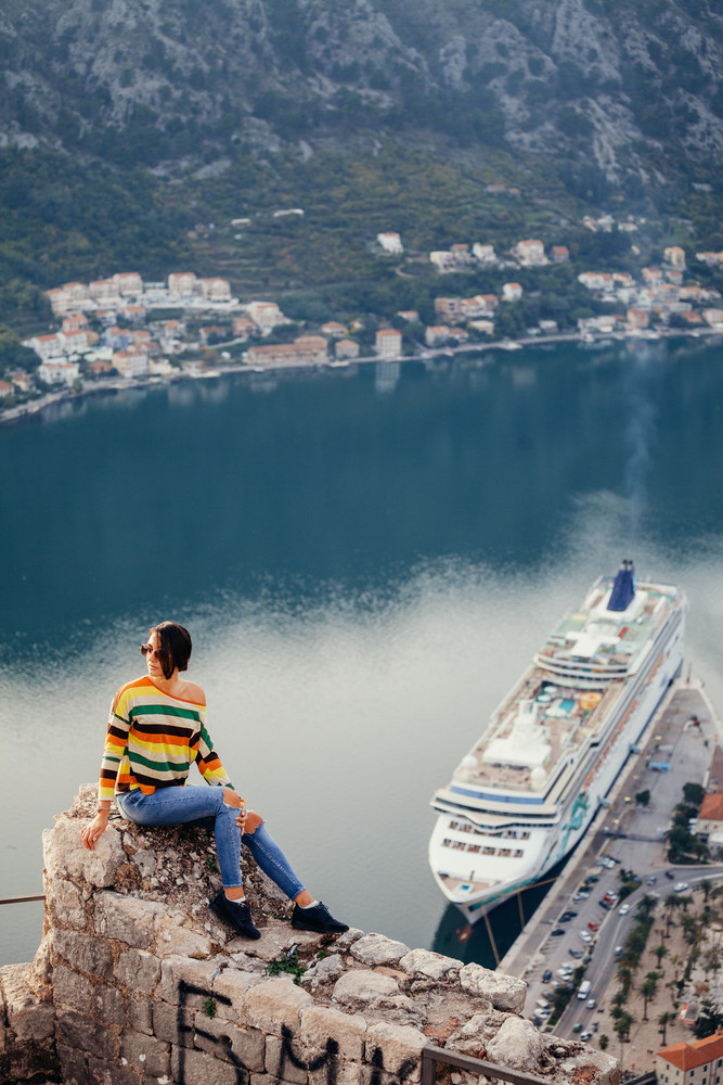 Official cruise excursions - photo of woman sitting on cliff looking down at cruise ship