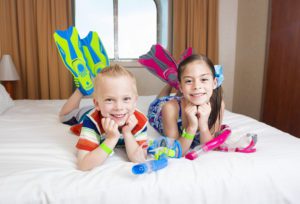 Choosing a cruise cabin-kids in pool gear lounging on bed of oceanview stateroom