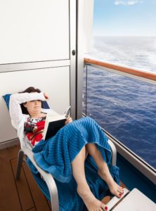 Choosing a cruise cabin - photo features woman reading book on stateroom balcony