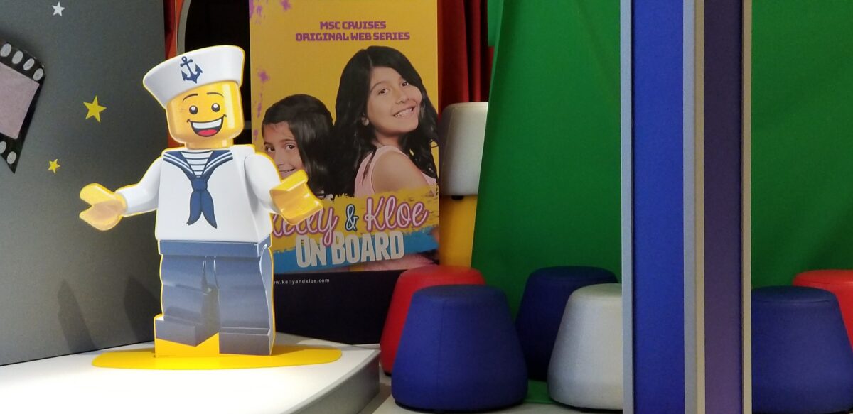 A grinning LEGO sailor figure with a sailor hat and anchor emblem stands on a yellow base in a play area.
