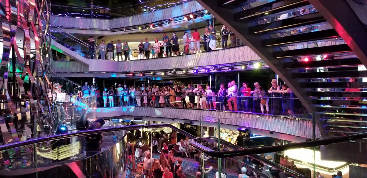 Crowds of guests lean over railings on three levels of a multi-story atrium, watching a performer below.