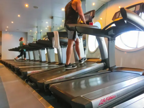 Guests on treadmills facing oceanview in cruise ship spa.