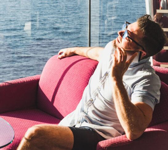 Photo of man in lounge using cell phone on a cruise while watching the ocean.