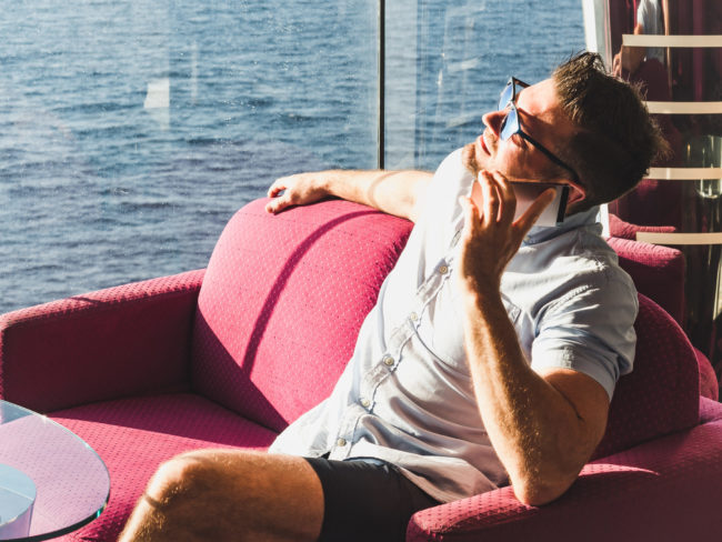 Photo of man in lounge using cell phone on a cruise while watching the ocean.
