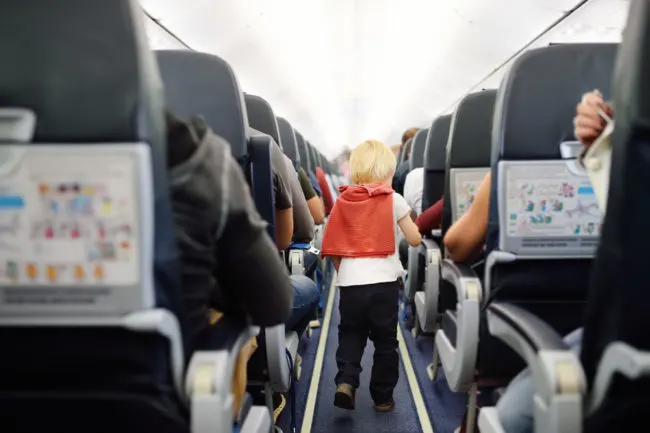 Flying With Kids | photo of small child walking down aisle of full airplane