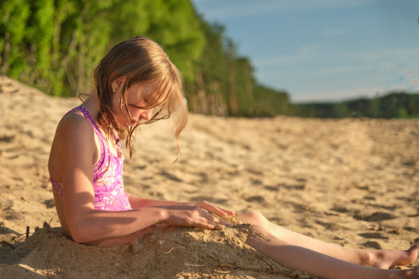 What Item Should You Bring in Your Beach Bag to Help Remove Sand From Your Skin? | photo of girl burying herself in the sand at the beach