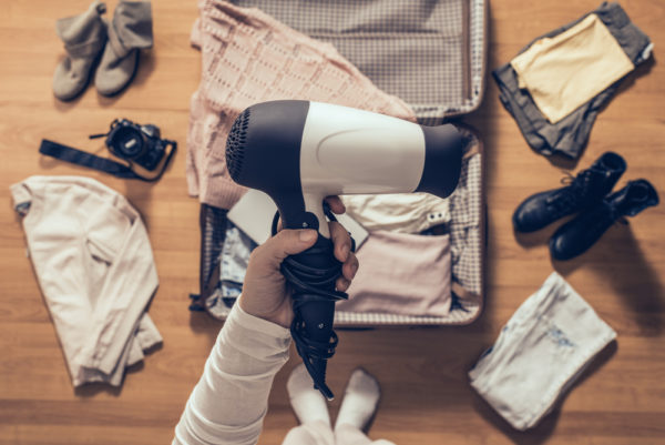 Do Cruise Ships Have Hair Dryers | woman holds hair dryer packing clothes in the open suitcase. 