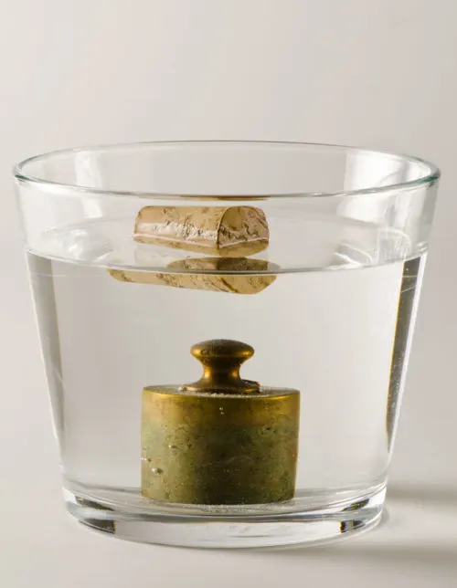 Why Do Cruise Ships Float | photo demonstrating Archimedes Principle -- floating cork vs Physics. A cork floats in water and  a antique weight that sinks. 