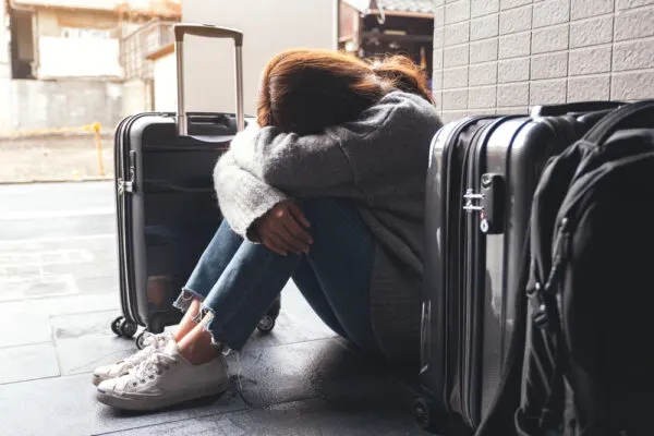 Photo of woman surrounded by luggage sitting on ground with head hidden in folded arms