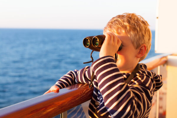 photo of adventurous little boy using small binoculars on cruise ship
