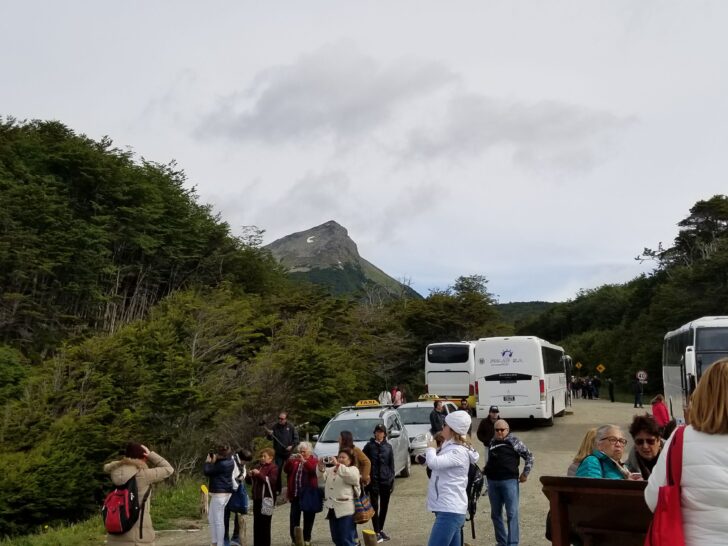 Photo of small crowd gathered at a popular tourist attraction in South America with a variety of large tour buses, smaller vans, and private taxis.