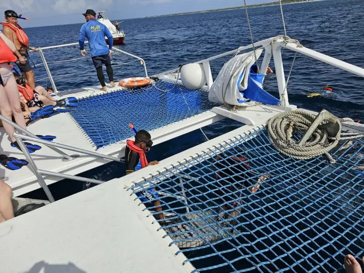 Photo of tourists on snorkeling excursion boat using stairs to enter water rather than jumping off side of boat.