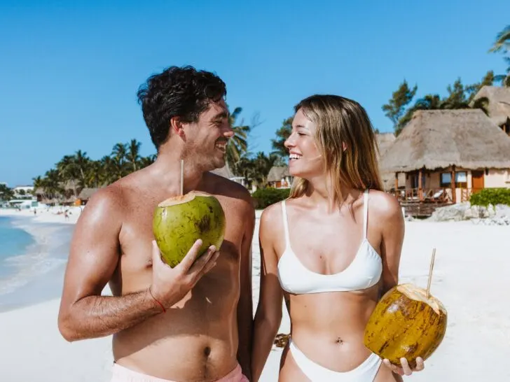 Photo of happy young couple walking on beach with coconut beverages.