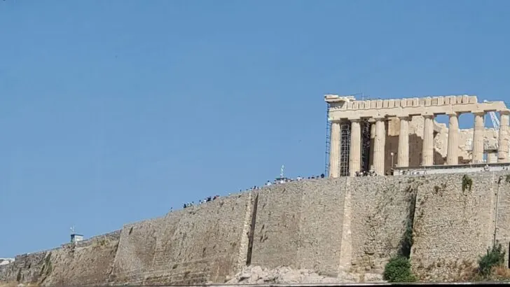 Best Times for a Mediterranean Cruise | The Parthenon, an ancient temple on the Acropolis in Athens, Greece, viewed from below with crowds of visitors along the base of the historic stone structure.