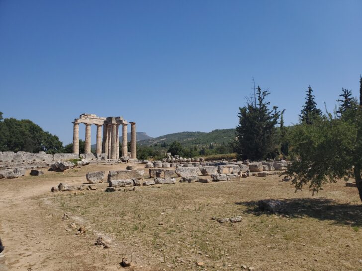 Ruins of the Temple of Zeus in Nemea, Greece, with standing columns and scattered stone remains in an open landscape.