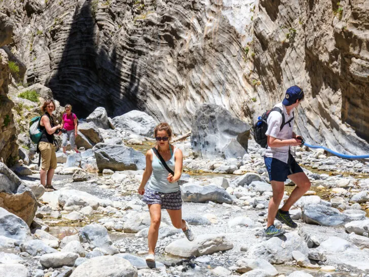 Photo of tourists scrabbling across rocks outside cave in Greece.