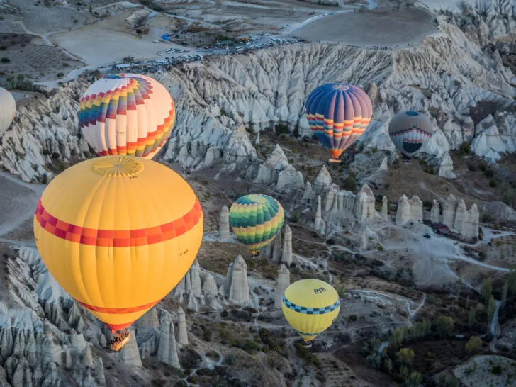 Aerial view of colorful hot air balloons drifting over the unique rock formations of Cappadocia, Turkey.