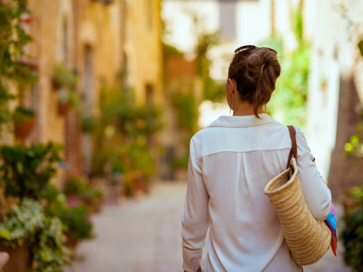 Photo of woman strolling through Tuscan village with straw day bag.