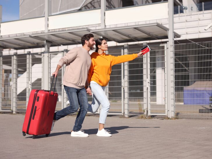 A couple running with a red suitcase and travel documents, appearing rushed as they hurry to their destination.