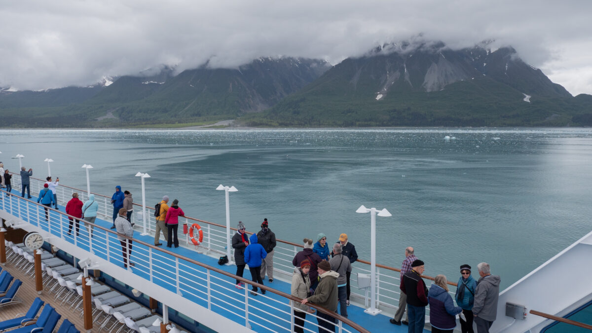 Cruise ship passengers bundled up on deck, admiring Alaska’s calm waters, surrounding glaciers, and misty mountains—one of the top unique cruise destinations for nature lovers.