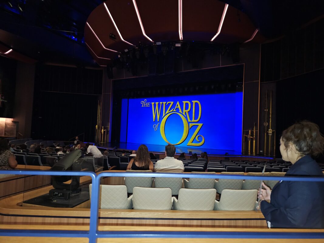 A view of the Icon of the Seas theater featuring a blue-lit stage with The Wizard of Oz title displayed, as attendees settle into their seats.