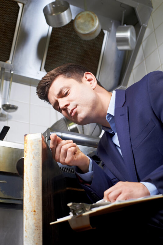 A sanitation officer conducting a detailed cleanliness check in a kitchen, ensuring compliance with food safety regulations.