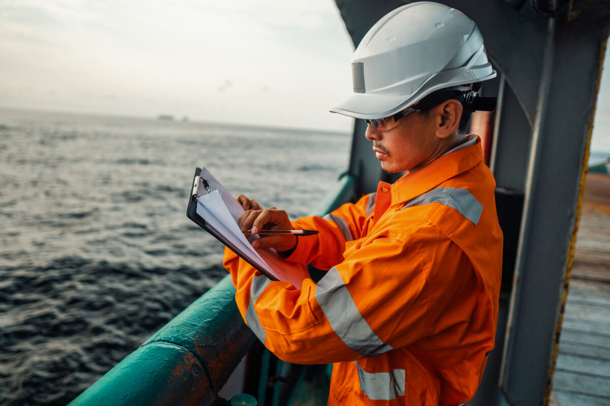 A cruise ship safety officer in protective gear documenting inspection details, ensuring sanitation and safety standards adherence.