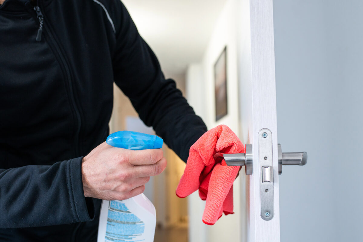 A person disinfecting a door handle with a spray bottle and cloth, highlighting the importance of sanitizing high-touch surfaces.