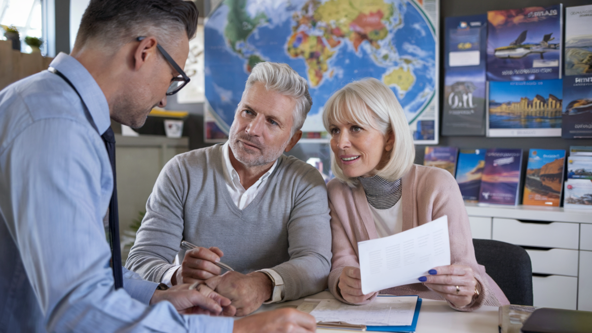 A travel agent consulting with a couple about their upcoming trip, with colorful travel posters and a world map decorating the office walls.