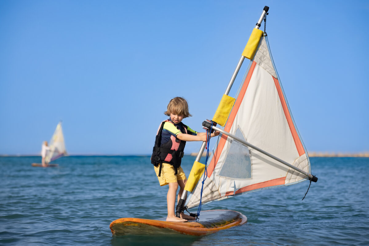 A boy in a life jacket windsurfing in calm waters, an example of the fun and active experiences families can enjoy on a cruise vacation.