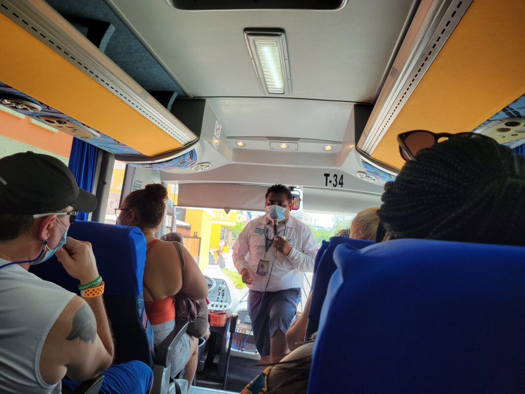 Passengers seated inside a tour bus, listening to a guide provide information about their upcoming excursion.