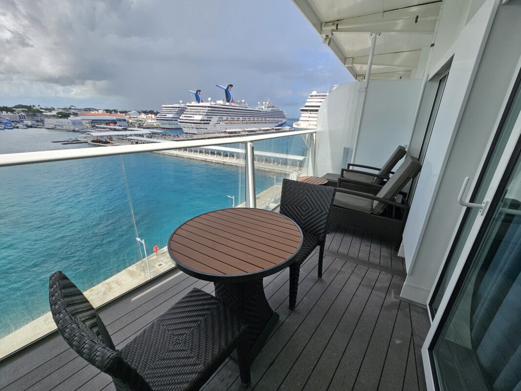 Cruise cabin balcony with two full-sized lounge chairs with side table and small dining table with two chairs.