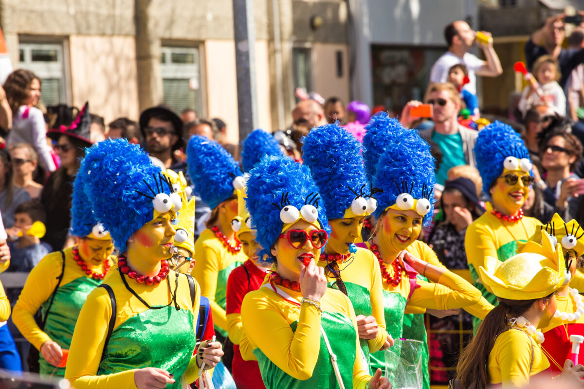 A group of carnival participants dressed in bright yellow and green costumes with blue wigs and oversized accessories parade through the streets during Cyprus Carnival.