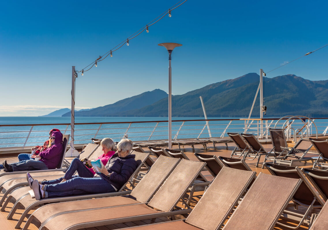 Cruise guests bundled in warm clothing enjoy Alaska’s views from the ship’s outdoor deck, proving that public decks can offer views just as stunning as a balcony cabin.