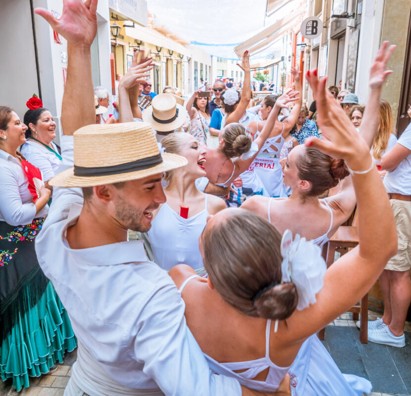 A man in a straw hat dances with a group of flamenco performers during the Feria de Málaga, capturing the excitement of this Mediterranean festival.