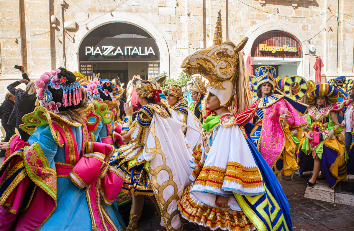 A group of dancers dressed in vibrant gold, pink, and blue costumes celebrates during a Malta Carnival.