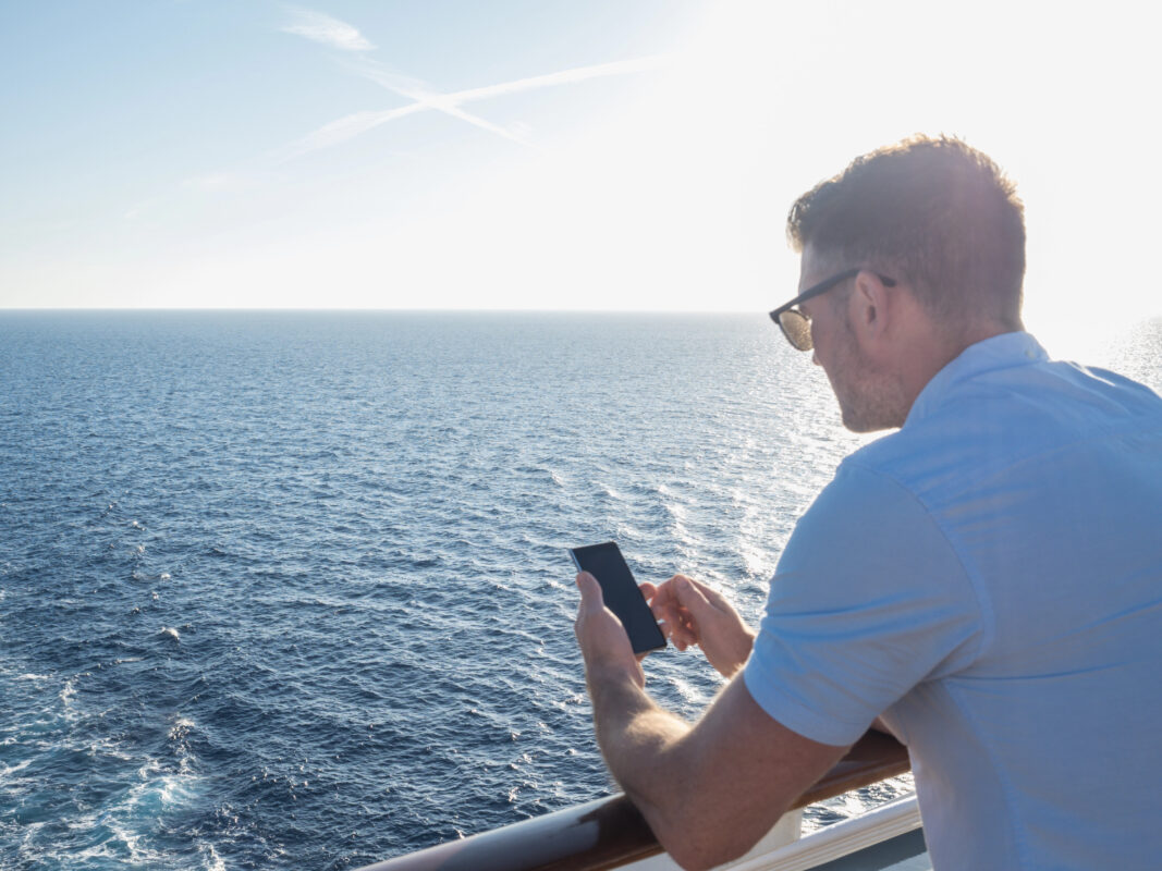 Staying connected at sea: man on cruise ship using mobile device over open water