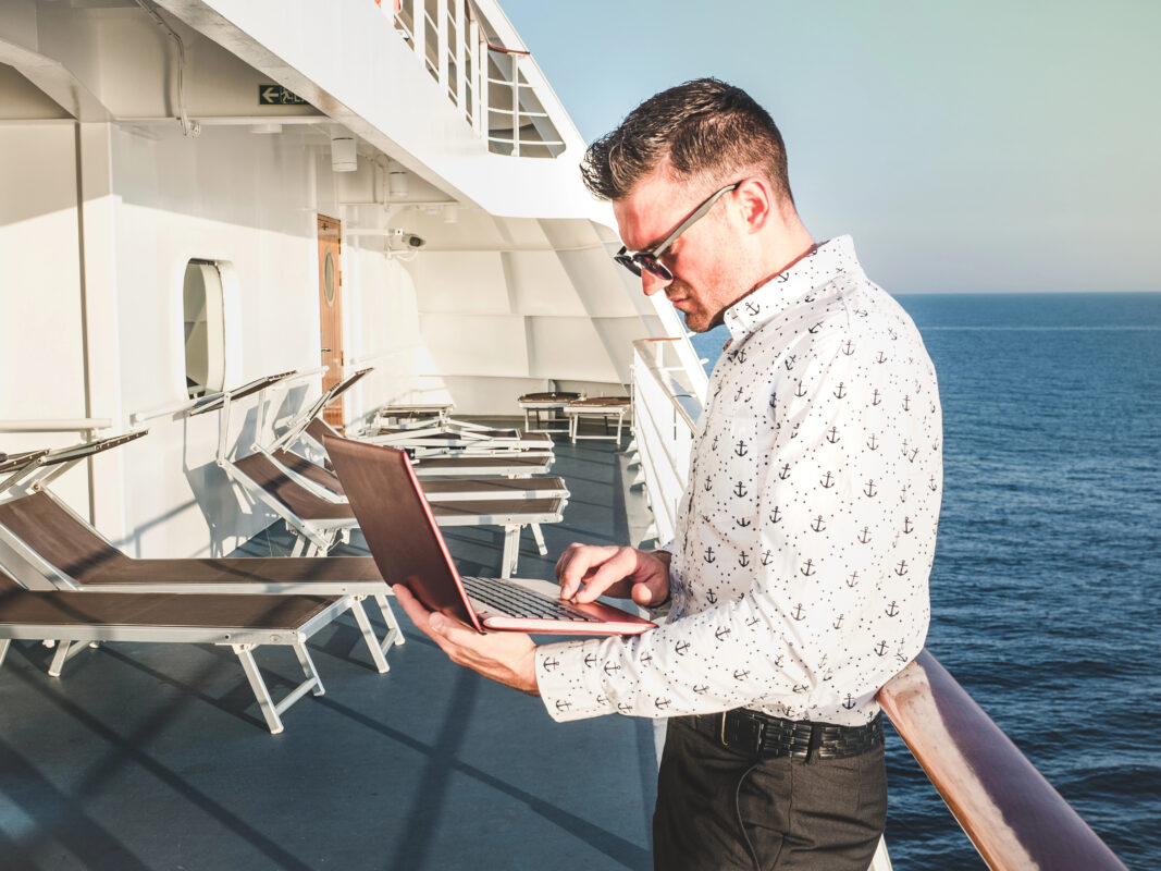 Man using a laptop on a cruise ship deck with ocean view