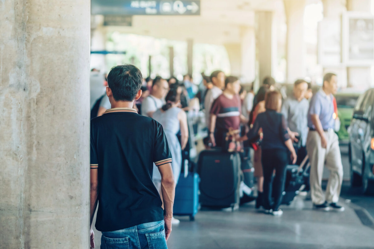 A man watches a packed curbside area where dozens of passengers scramble for ground transportation.