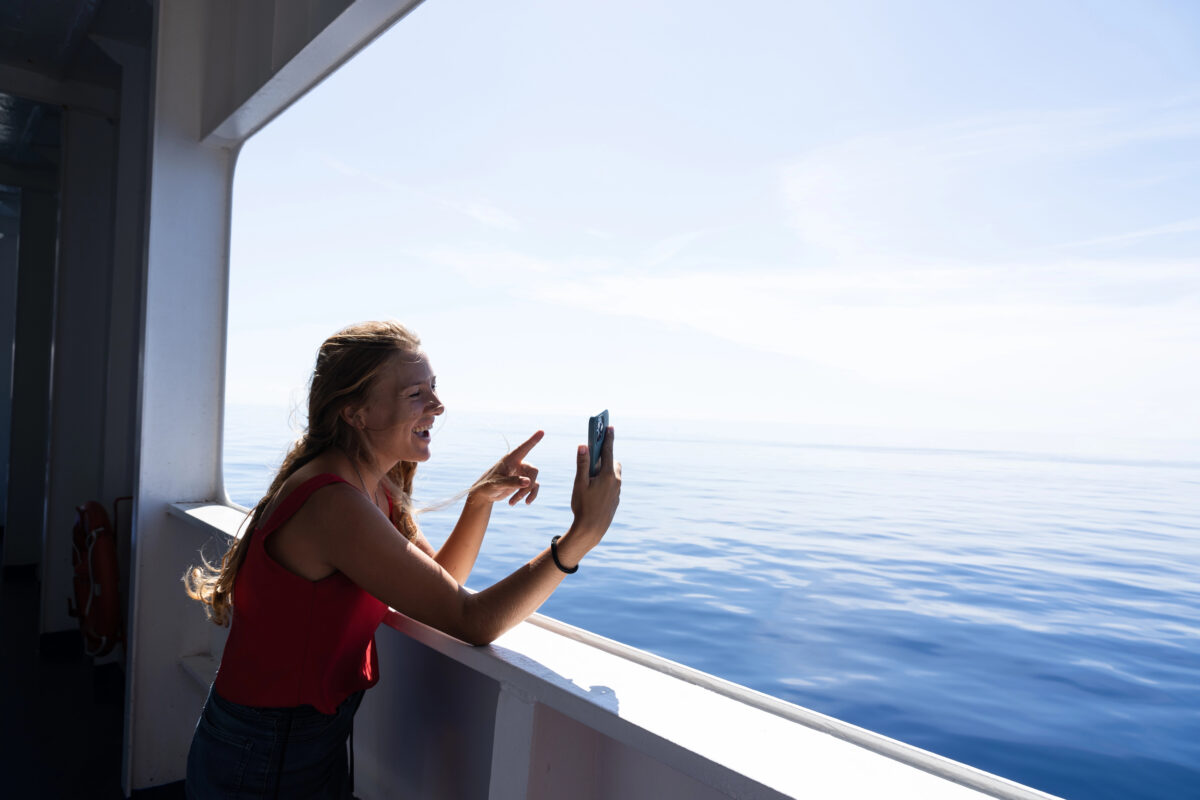 Using Wi-Fi for a video call on a cruise: woman smiling at her phone on deck