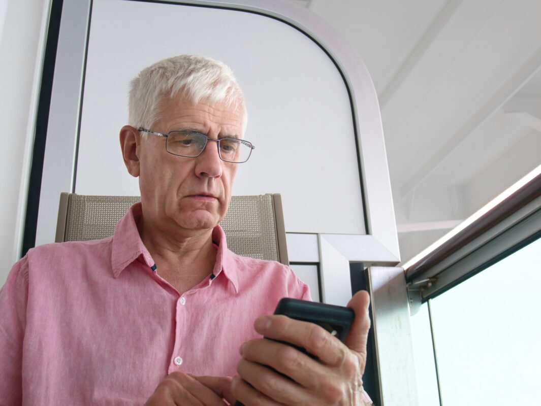 Slightly puzzled senior man using smartphone on a cruise ship balcony