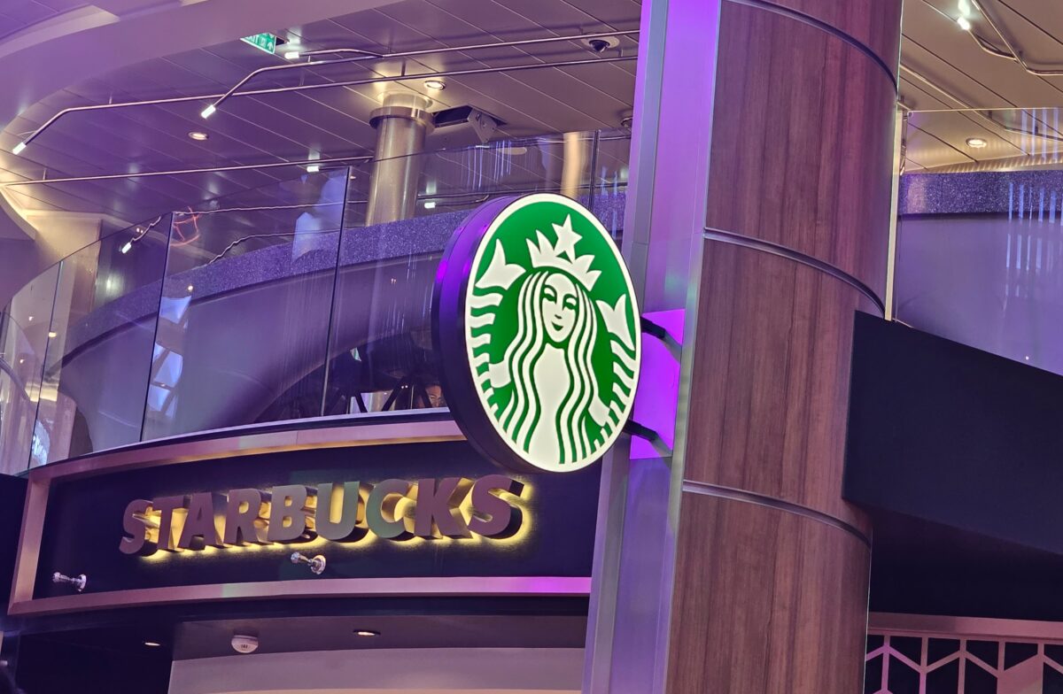 Cruise ship interior featuring a Starbucks location with the brand’s green siren logo and polished metal accents.