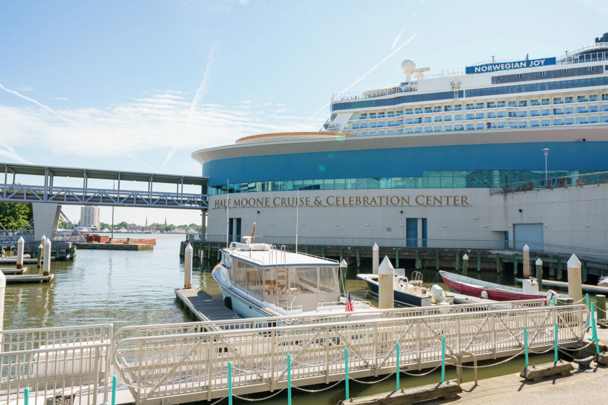 Cruise ship at the Half Moone Cruise Center in Norfolk, VA, with docked boats and waterfront walkway visible.