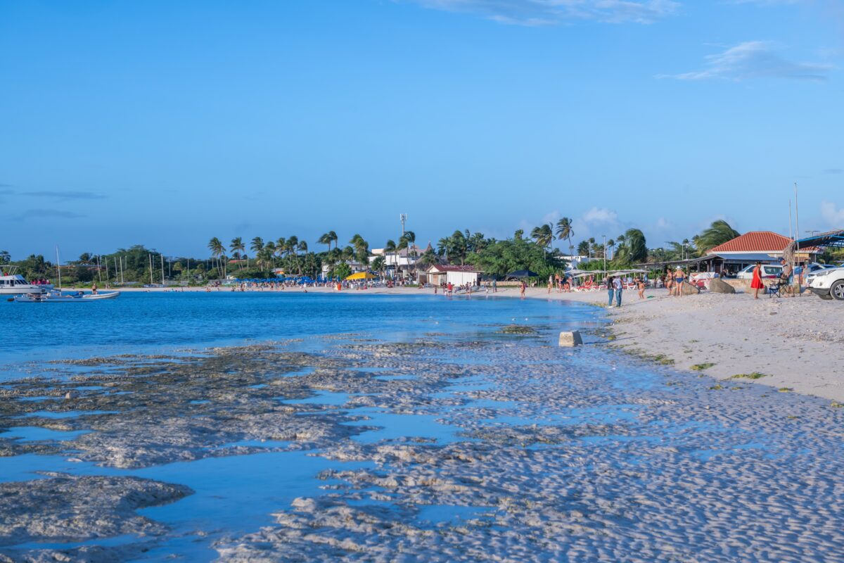 Photo of Surfside Beach showing shallow water, sandy shoreline, and a mix of locals and tourists along the beachfront.