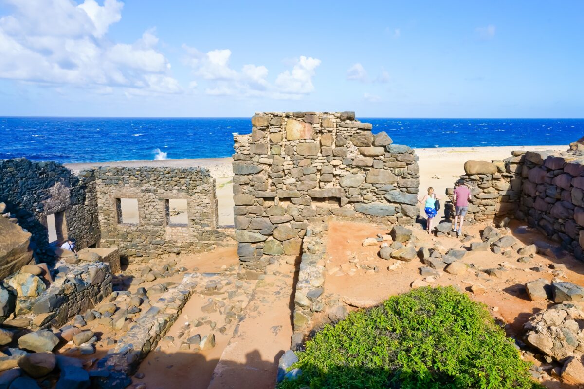 View of the Bushiribana Gold Mill Ruins in Aruba with crumbling stone walls overlooking the rocky northern coastline and bright blue sea.