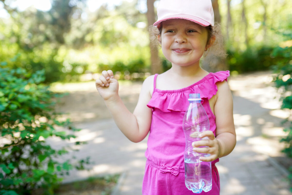Happy child with a baseball cap holding water while walking outdoors.