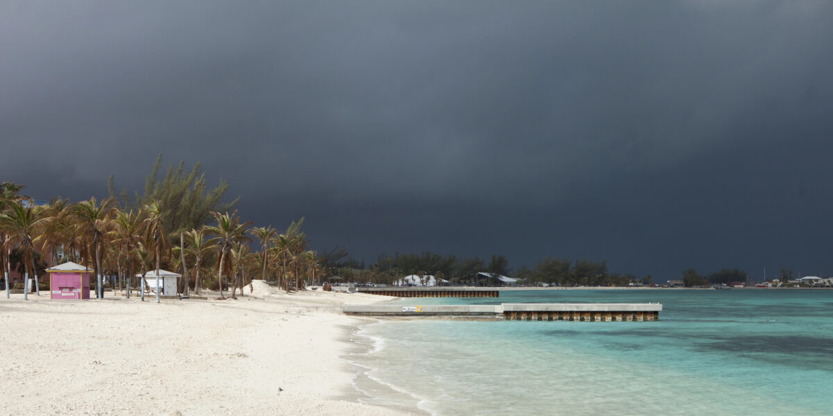 A desolate beach in the Bahamas under dark, threatening clouds from an oncoming hurricane—illustrating the weather risks associated with a Caribbean cruise during hurricane season.