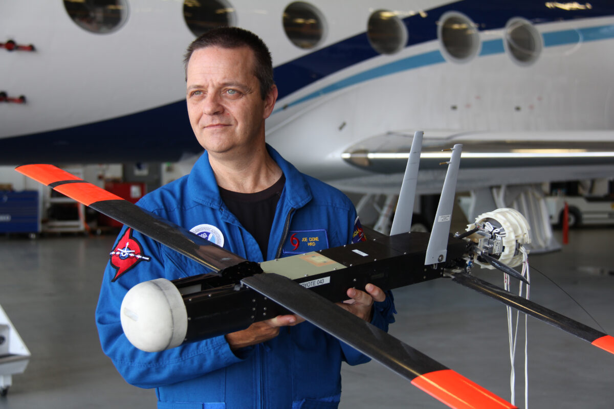 Man in blue flight suit displays compact drone used in hurricane tracking operations by NOAA.