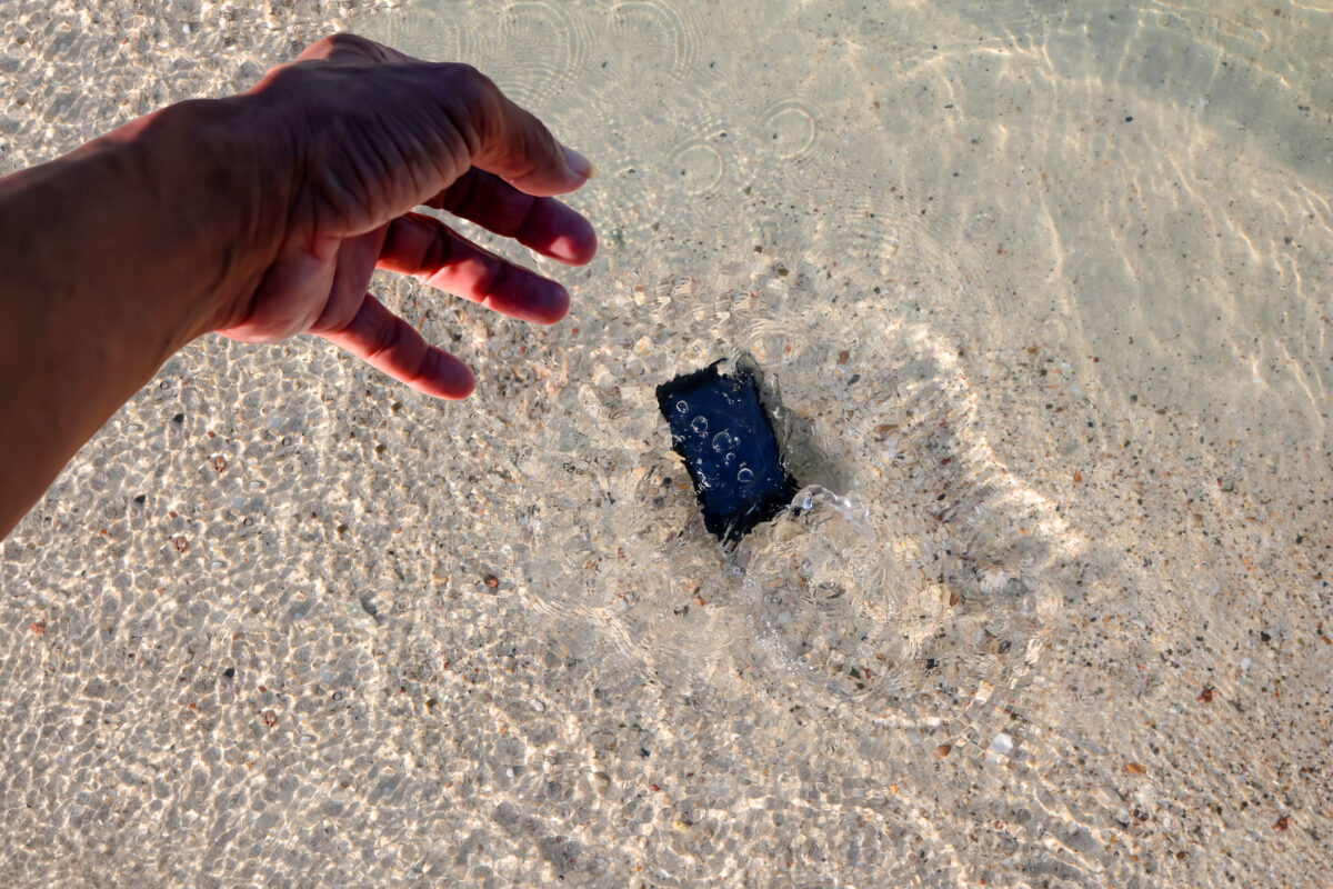 Smartphone sinking in clear ocean water, illustrating the importance of using a waterproof case during cruise shore excursions.